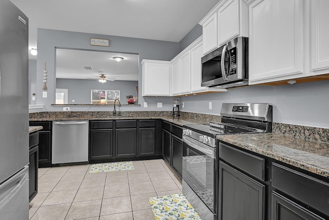 kitchen with dark stone counters, stainless steel appliances, dark cabinetry, white cabinetry, and a sink