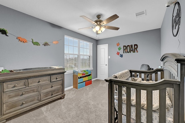 bedroom featuring visible vents, a ceiling fan, light carpet, a nursery area, and baseboards