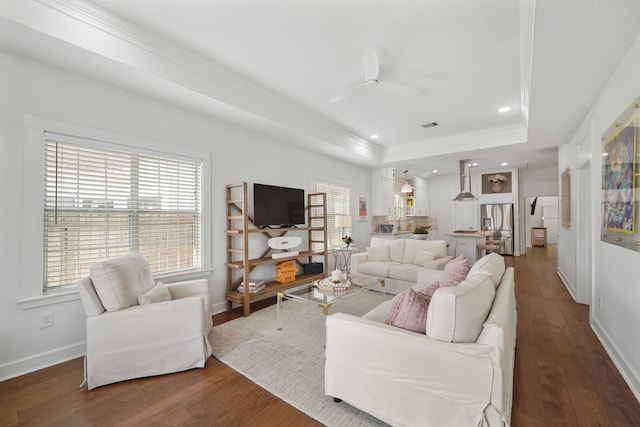 living area with a ceiling fan, a raised ceiling, baseboards, and wood finished floors