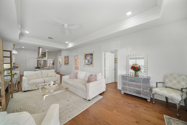 living room with a tray ceiling, crown molding, recessed lighting, and wood finished floors