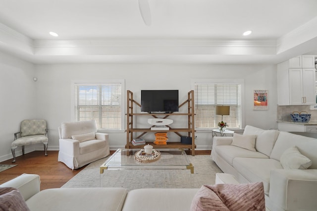 living room with light wood-type flooring, a tray ceiling, ornamental molding, and baseboards