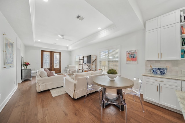 living area with a tray ceiling, dark wood-style flooring, visible vents, and french doors