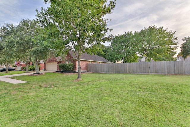 view of yard with concrete driveway, an attached garage, and fence