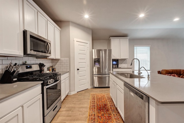 kitchen featuring stainless steel appliances, a sink, light wood-style floors, white cabinets, and an island with sink