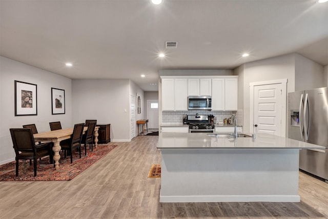 kitchen with visible vents, white cabinets, a kitchen island with sink, stainless steel appliances, and light countertops