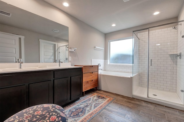 bathroom with a garden tub, a sink, wood tiled floor, double vanity, and a stall shower