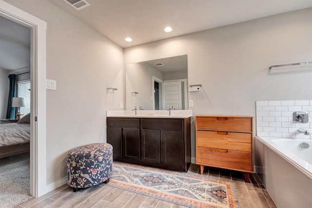 ensuite bathroom with double vanity, visible vents, connected bathroom, a garden tub, and wood finish floors