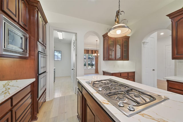 kitchen featuring stainless steel appliances, arched walkways, glass insert cabinets, and hanging light fixtures