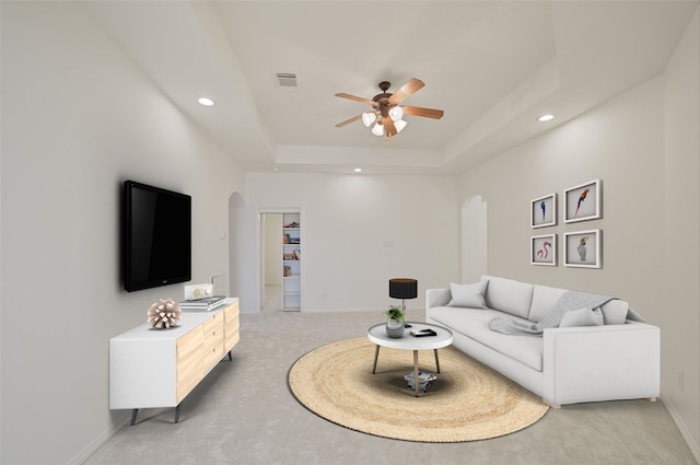 living area featuring arched walkways, visible vents, light carpet, and a tray ceiling