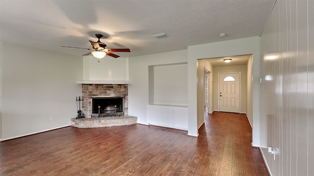 unfurnished living room with dark wood-style flooring, a fireplace, visible vents, a ceiling fan, and a textured ceiling