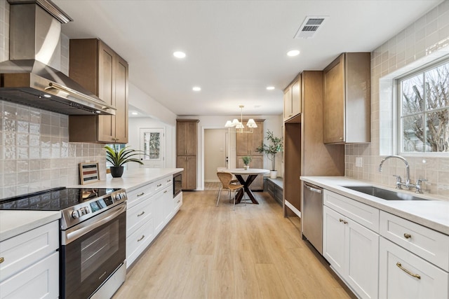 kitchen with wall chimney range hood, stainless steel appliances, a sink, and light countertops