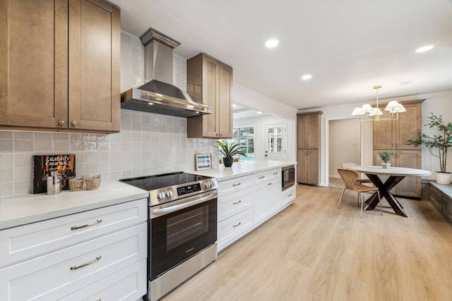 kitchen featuring white cabinets, stainless steel electric range, built in microwave, light countertops, and wall chimney range hood