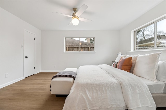 bedroom with ceiling fan, multiple windows, wood finished floors, and baseboards