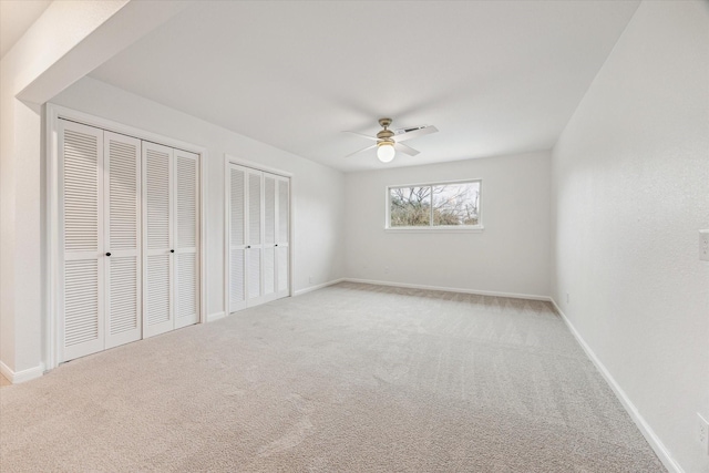 unfurnished bedroom with a ceiling fan, light carpet, baseboards, and two closets