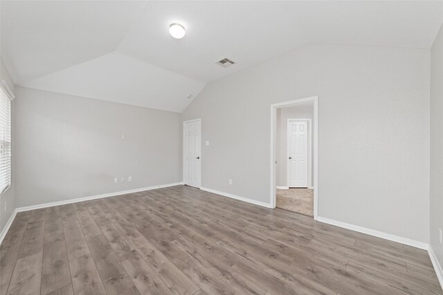 spare room with lofted ceiling, visible vents, and wood finished floors