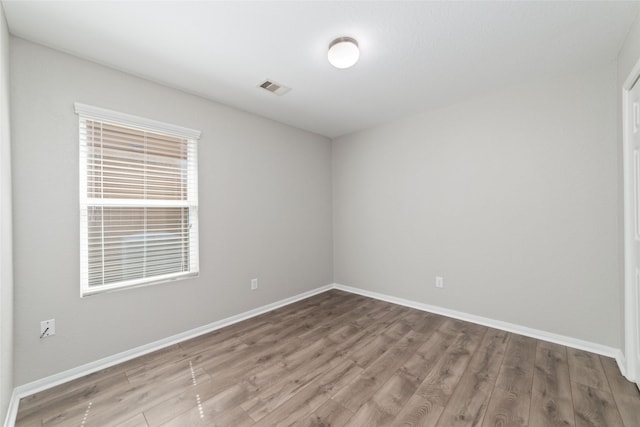 empty room with wood finished floors, visible vents, and baseboards