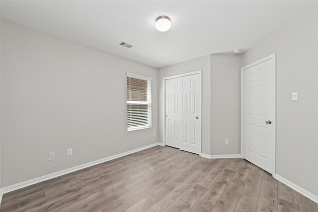 unfurnished bedroom with a closet, baseboards, visible vents, and light wood finished floors