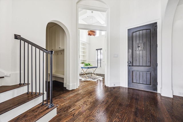 foyer with dark wood-style floors, arched walkways, and stairs