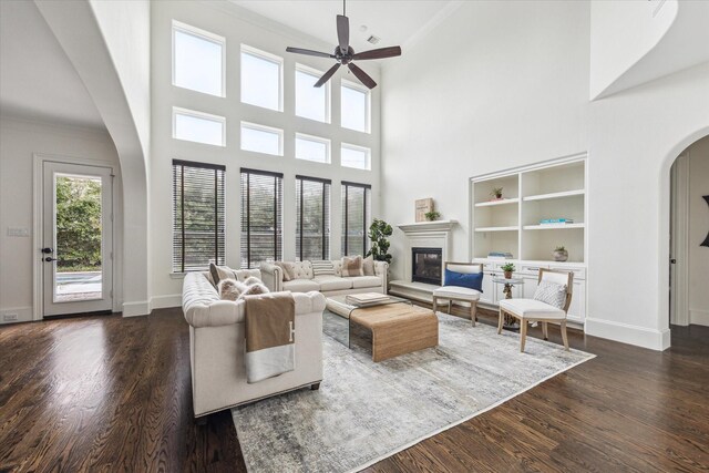 living room featuring baseboards, arched walkways, dark wood finished floors, and a glass covered fireplace