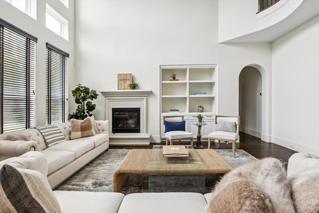 living room with arched walkways, a high ceiling, dark wood-style flooring, and a glass covered fireplace