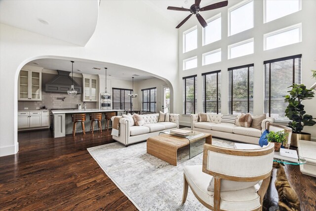 living room featuring dark wood-style floors, arched walkways, a ceiling fan, and baseboards