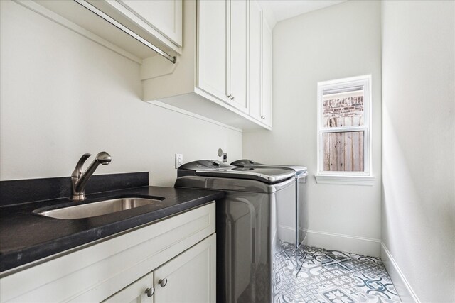 clothes washing area with cabinet space, baseboards, a sink, and washing machine and clothes dryer