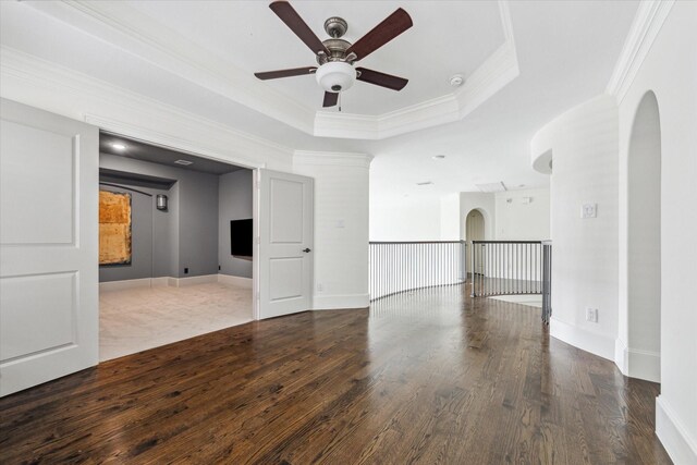 unfurnished room featuring ornamental molding, wood finished floors, arched walkways, and a raised ceiling