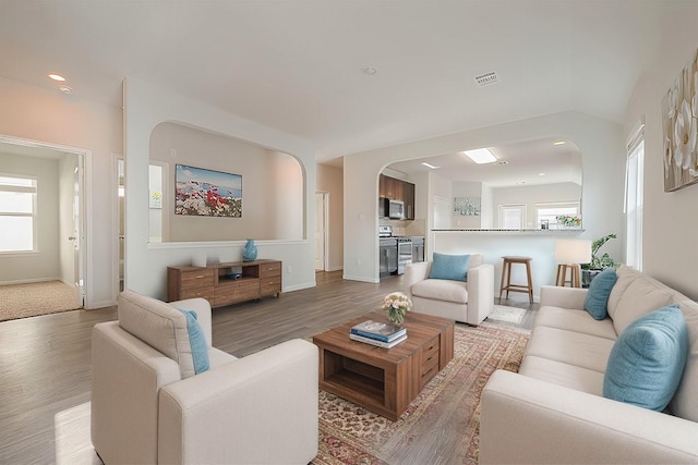 living area featuring visible vents, baseboards, light wood-type flooring, recessed lighting, and arched walkways