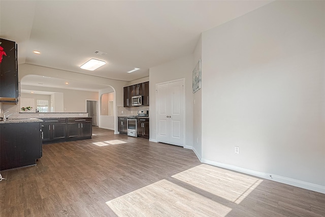 interior space featuring decorative backsplash, arched walkways, appliances with stainless steel finishes, and wood finished floors