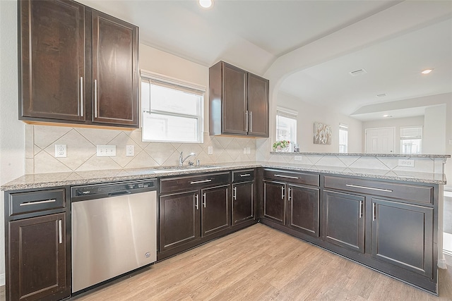 kitchen featuring backsplash, a peninsula, stainless steel dishwasher, light wood-style floors, and a sink