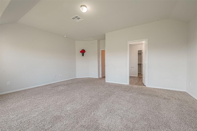 spare room with light carpet, visible vents, baseboards, and vaulted ceiling