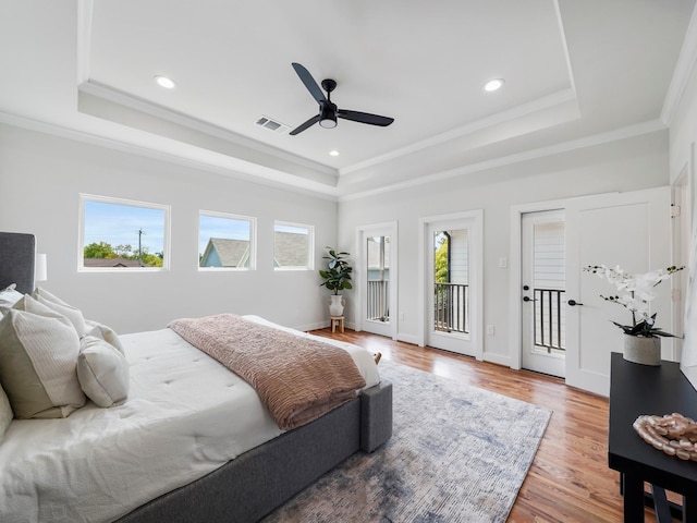 bedroom featuring visible vents, a tray ceiling, wood finished floors, and ornamental molding