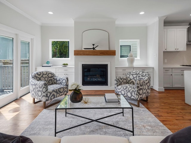 living area with recessed lighting, light wood-type flooring, a glass covered fireplace, and crown molding