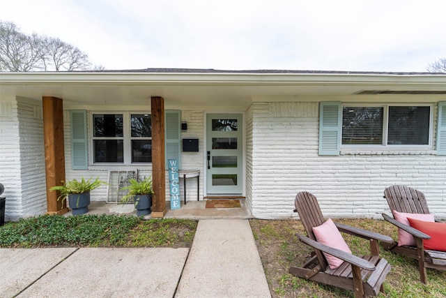 view of exterior entry with a porch and brick siding