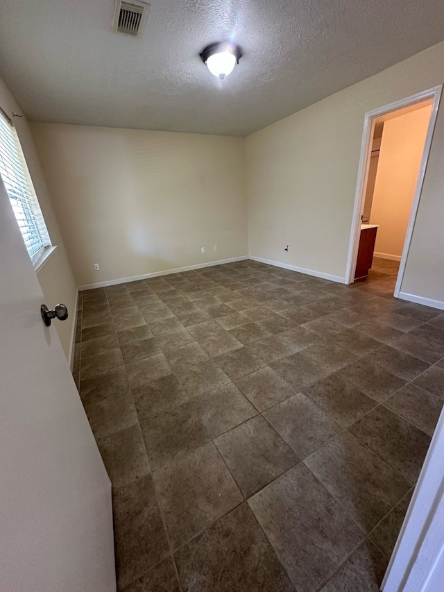 spare room with visible vents, a textured ceiling, baseboards, and dark tile patterned flooring