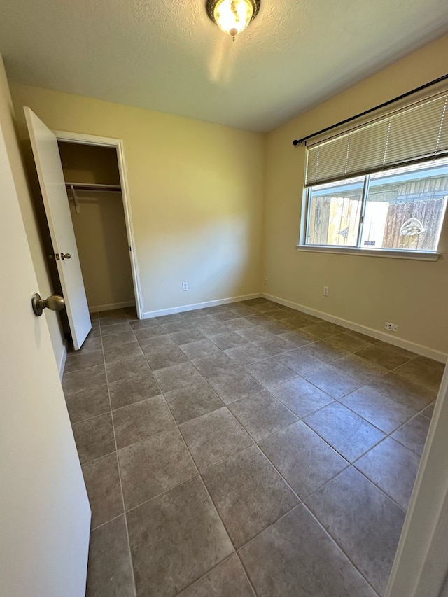 unfurnished bedroom featuring baseboards, a closet, dark tile patterned floors, and a textured ceiling