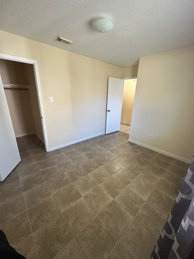 unfurnished bedroom with a textured ceiling, visible vents, and baseboards