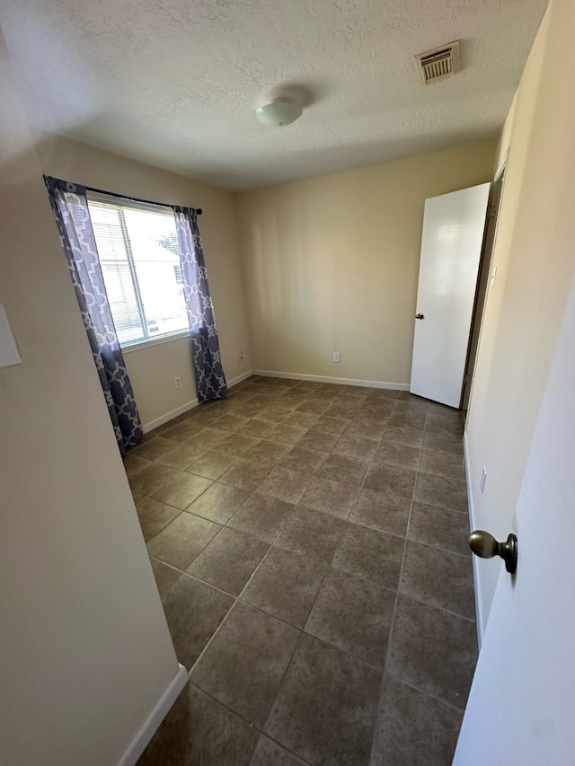 unfurnished room featuring dark tile patterned flooring, a textured ceiling, visible vents, and baseboards