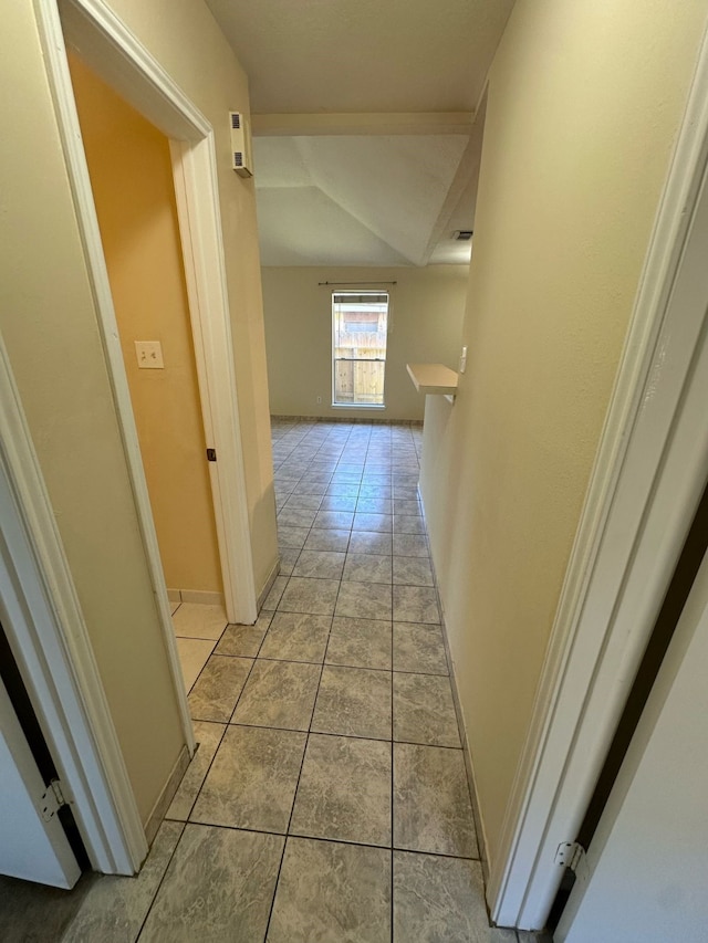 corridor featuring baseboards, light tile patterned floors, and lofted ceiling