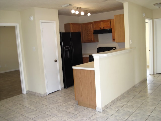 kitchen with light countertops, light tile patterned floors, a peninsula, black refrigerator with ice dispenser, and under cabinet range hood