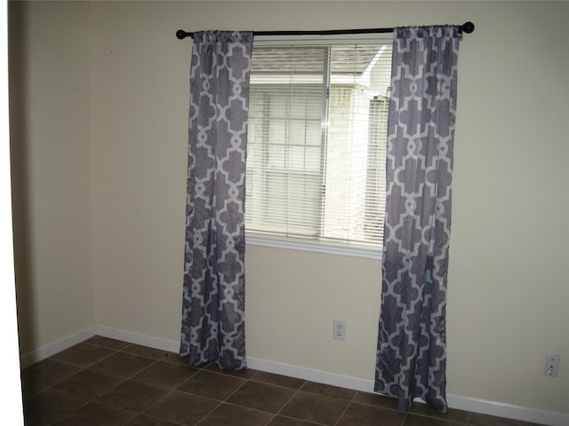unfurnished room featuring dark tile patterned floors and baseboards