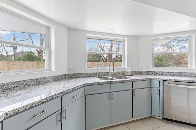 kitchen with light tile patterned floors, stainless steel dishwasher, a sink, and gray cabinetry