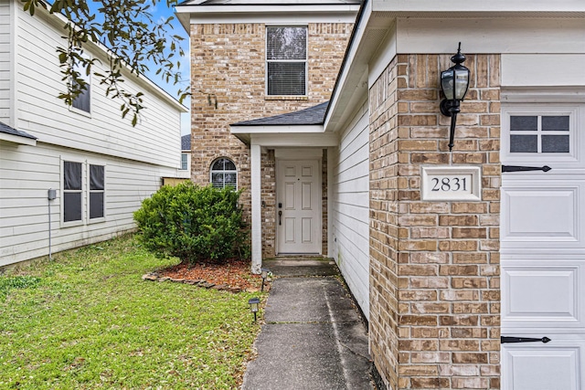 view of exterior entry with an attached garage, a yard, and brick siding