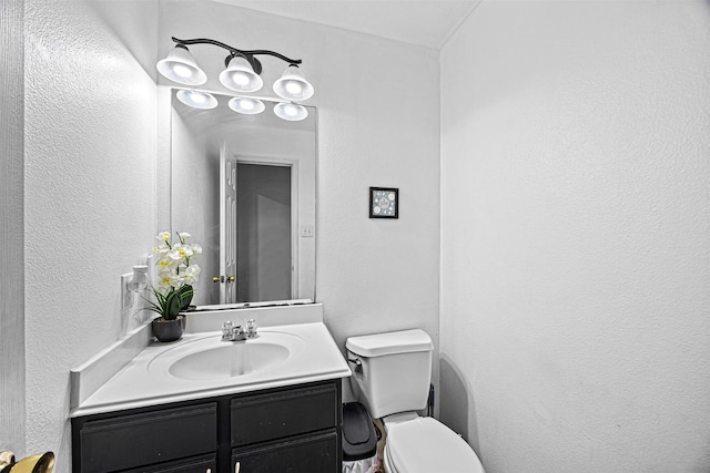 bathroom featuring toilet, a textured wall, and vanity