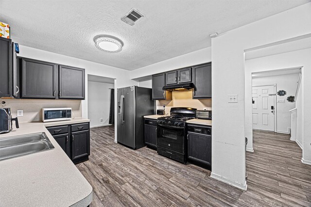 kitchen featuring under cabinet range hood, visible vents, light countertops, black range with gas stovetop, and stainless steel fridge with ice dispenser