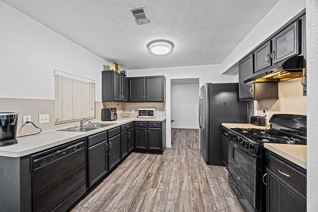 kitchen featuring visible vents, light countertops, a sink, under cabinet range hood, and black appliances