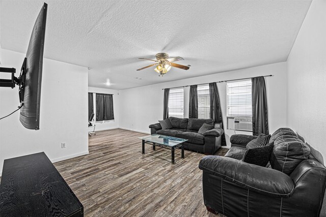 living area with ceiling fan, a textured ceiling, wood finished floors, cooling unit, and baseboards