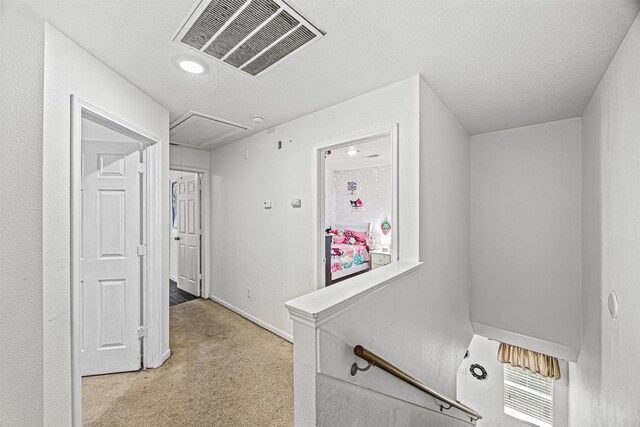 hall featuring visible vents, attic access, light carpet, a textured ceiling, and baseboards