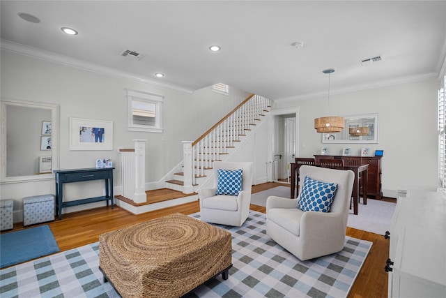 living room with stairs, wood finished floors, visible vents, and crown molding