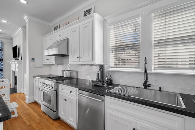 kitchen featuring white cabinets, dark countertops, stainless steel appliances, under cabinet range hood, and a sink